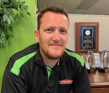 brown haired man in front of desk and green wall