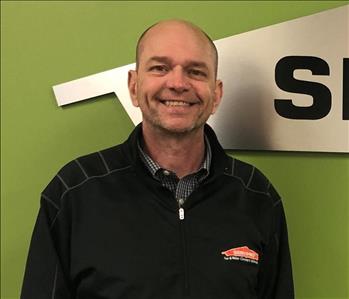 man in black shirt smiling in front of green and silver wall