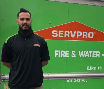 Man with black hair and beard standing in front of green van